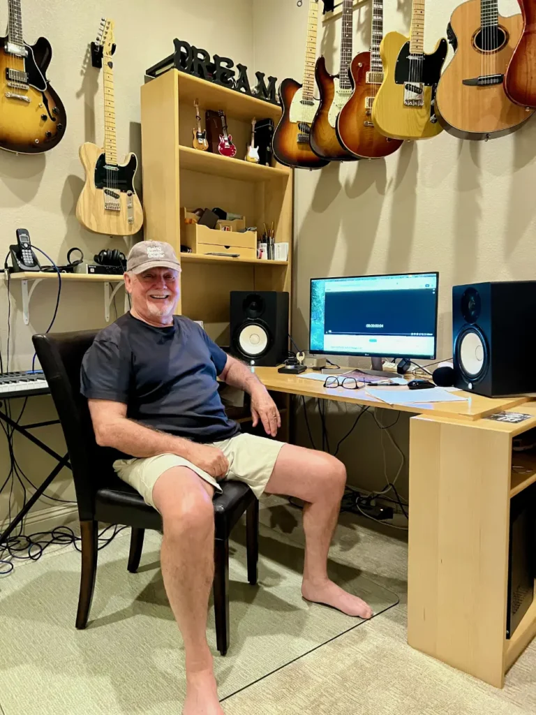 Image of Tim Manion sitting at his computer desk surrounded by guitars